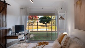 A bedroom with a large window, a desk with a computer, a bed with a blanket, and a hanging light fixture. - Sunset Retreat-amaxing views over Mt Franklin (Franklinford)