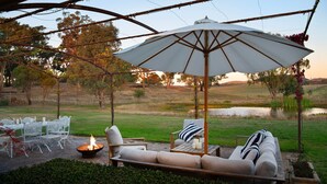 An outdoor seating area with a fire pit, white chairs, and a large umbrella. - Sunset Retreat-amaxing views over Mt Franklin (Franklinford)