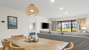 Una sala de estar moderna con una mesa de comedor de madera, un sofá gris y un ventanal con cortinas.