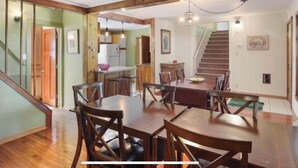 A spacious dining area with a wooden table and chairs, a kitchen in the background, and a staircase leading upstairs. - Cozy Large House, Big Porch, Fire Pit, Live Music Brewery, Heart of Lake Ann! (Lake Ann)
