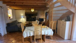 A cozy dining area with a table set for four, wooden chairs, a stone fireplace, and a television on a stand.