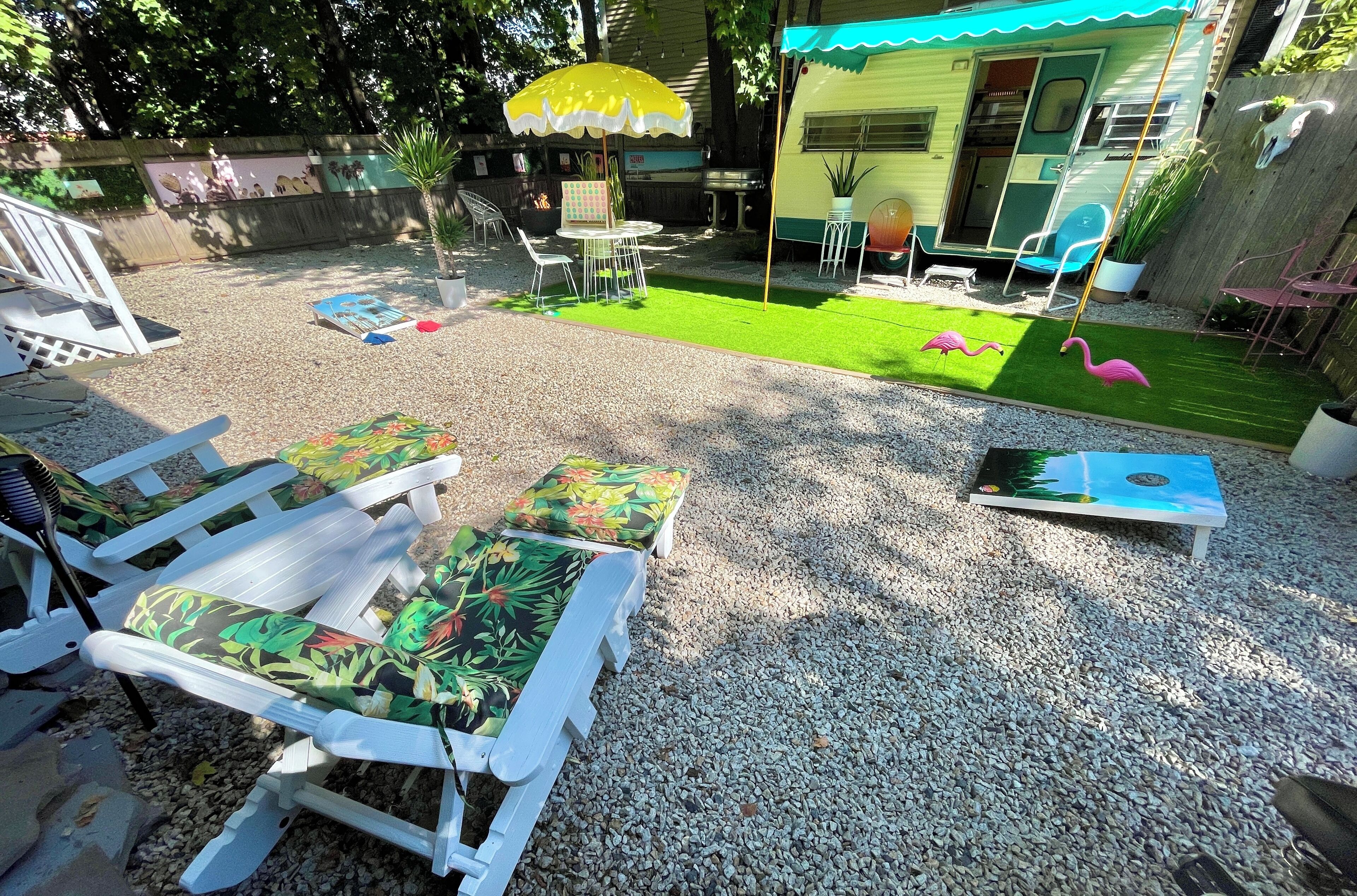 Een achtertuin met een terras, een klein gazon en een aanhangwagen.