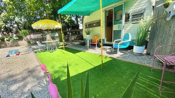 A backyard with artificial grass, a patio area with chairs, and a covered seating area.