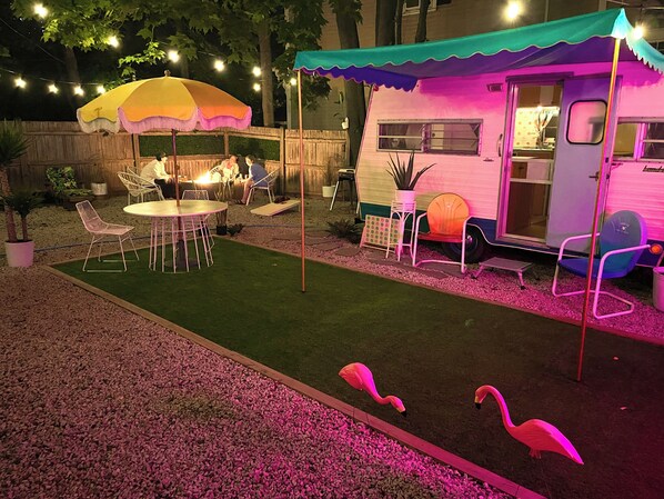 A patio with a table and chairs, a small fire pit, and a colorful canopy. - Vintage Glamper Oasis in Downtown Dover, walk to downtown and Henry Law Park (Dover)