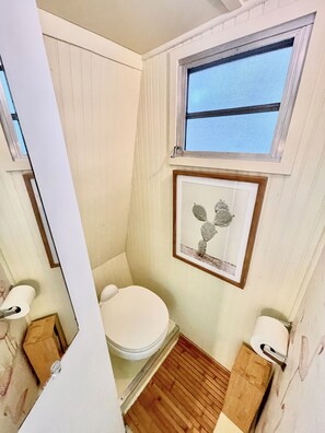 A small, compact bathroom with a toilet, a window, and a framed picture on the wall. - Vintage Glamper Oasis in Downtown Dover, walk to downtown and Henry Law Park (Dover)