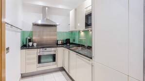 A compact kitchen with a built-in oven, a stainless steel range hood, a microwave, and a sink. - Closetoharrods - Closetohydepark - 2 bed House (London)