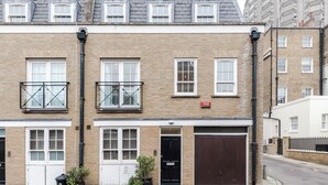 A two-story building with a brick facade, white-framed windows, and a black door. - Closetoharrods - Closetohydepark - 2 bed House (London)