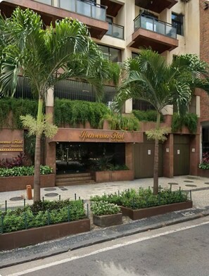 Un hotel con un letrero que dice 'Panama Flat Hotel Residencia'. Hay palmeras y un área pavimentada con macetas.