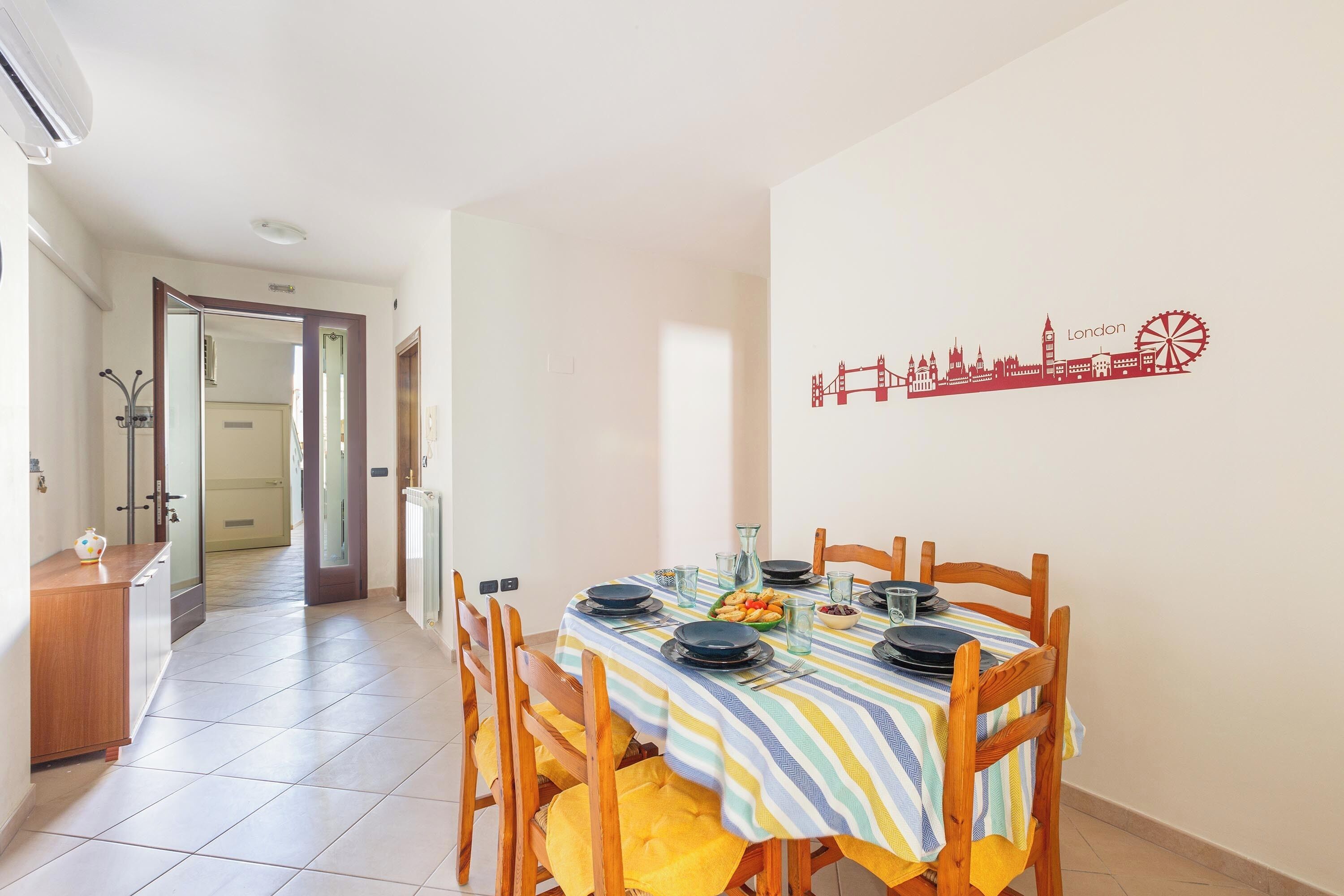 A dining area with a table set for four, a cityscape wall art, and a hallway leading to another room.