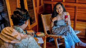 A wooden interior with a person sitting on a wicker chair, holding a drink. - Villa Mayu (Karangasem)