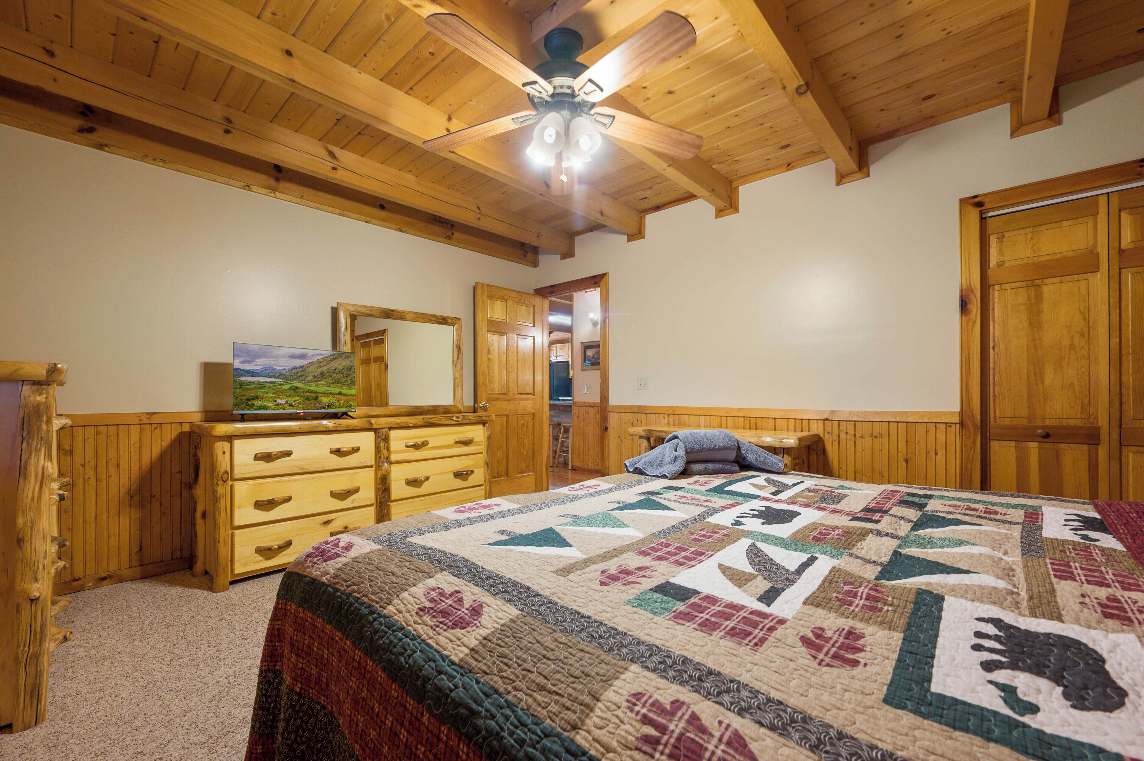 A bedroom with a wooden ceiling, a bed with a quilt, a dresser, a mirror, and a door.