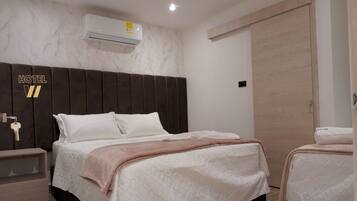 A hotel room with a large bed, a bedside table, an air conditioning unit, and a wardrobe.