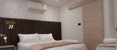 A hotel room with a large bed, a bedside table, an air conditioning unit, and a wardrobe.