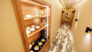 Un couloir avec une étagère en bois où sont exposées différentes tasses et une machine à café.
