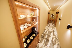 A hallway with a wooden shelf unit displaying various cups and a coffee maker. - HOTEL W Santa Marta (Santa Marta)