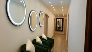 Un corridoio con tre poltrone verdi e tre specchi a parete con cornice illuminata.