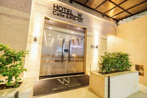 The entrance to HOTEL W with a clear sign above the door, a doormat with the hotel's name, and a potted plant to the right. - HOTEL W Santa Marta (Santa Marta)