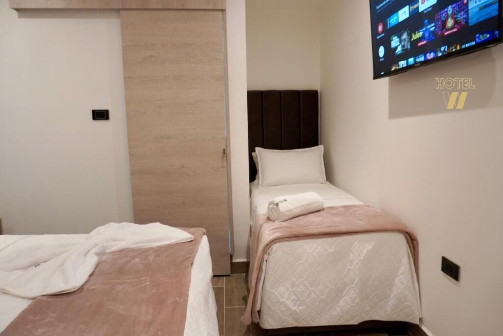 A hotel room with two beds, a television mounted on the wall, and a wooden door.