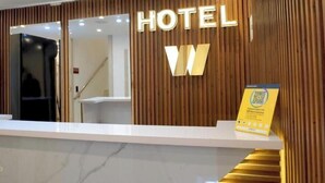 Una reception hotel con parete in legno, un'ampia insegna illuminata con la scritta 'HOTEL' e un cartello con un codice QR sulla destra.