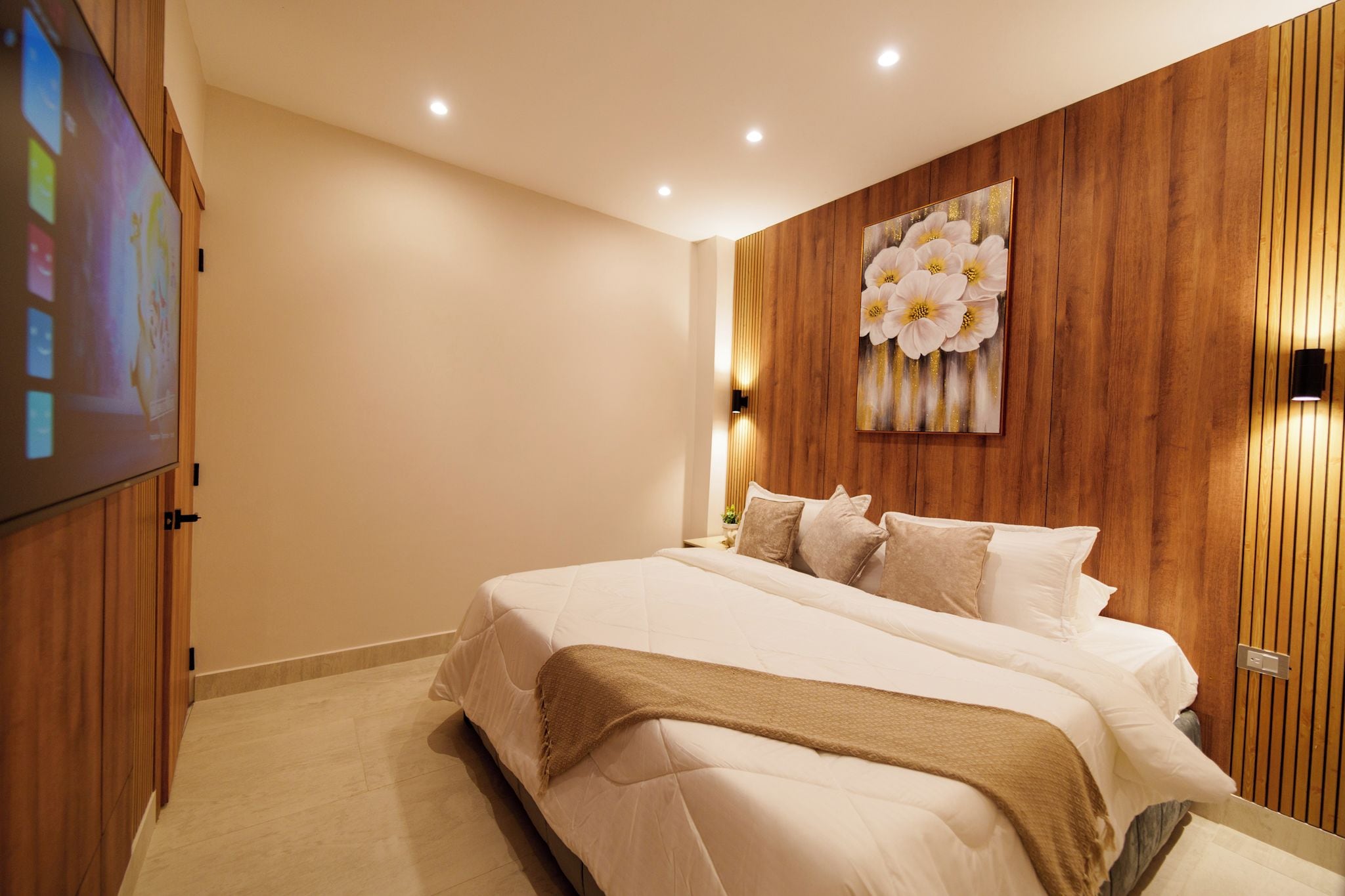 A bedroom with a large bed, wooden paneling on the walls, a flat-screen TV, and a floral artwork above the bed.