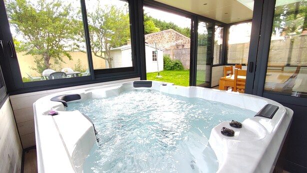 Ein Whirlpool mit Blick auf einen Garten und ein Haus durch große Fenster.
