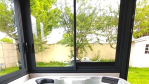 Ein Whirlpool mit Blick auf einen Garten und ein Haus, durch große Fenster sichtbar.