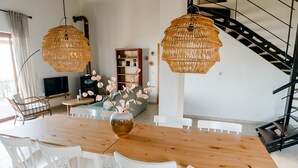 A modern living room with a wooden dining table, white chairs, and wicker pendant lights. - Beautiful Family Home With Breathtaking View of the sea and the City of Kalamata (Perivolakia)