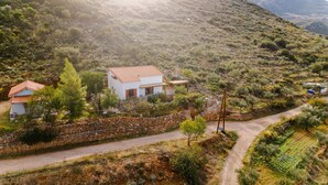A rural house with a stone wall, a small attached structure, and a dirt road. - Beautiful Family Home With Breathtaking View of the sea and the City of Kalamata (Perivolakia)