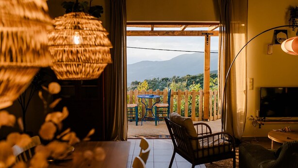 A cozy living room with a view of mountains, a dining area with a table and chairs, and a TV on the wall. - Beautiful Family Home With Breathtaking View of the sea and the City of Kalamata (Perivolakia)