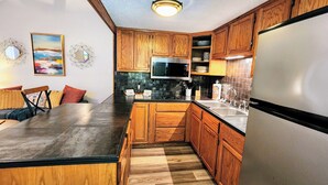 A modern kitchen with wooden cabinets, a stainless steel refrigerator, a microwave, and a dining area with a table and chairs.