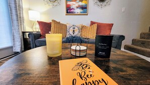 A cozy living room with a wooden coffee table, a yellow candle, a black candle, and a 'Bee Happy' sign.