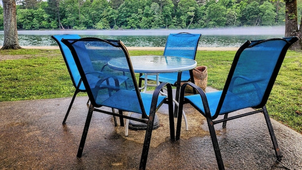 A table and chairs set outdoors with a view of a lake and forest.