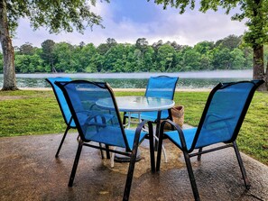A table and chairs set outdoors with a view of a lake and forest.