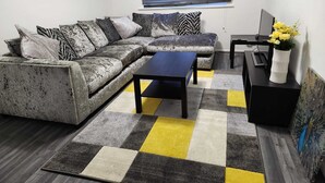 Un salon moderne avec un canapé d’angle gris, une table basse noire et un tapis à carreaux.