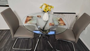 Un espace repas moderne avec une table en verre, deux chaises rembourrées et un vase de fleurs.