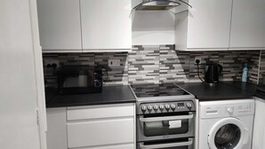 Une cuisine compacte avec des meubles blancs, un four à micro-ondes, une cuisinière et un lave-linge.