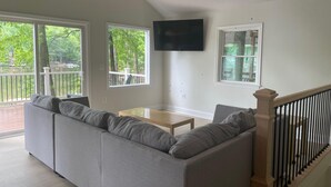 A spacious living room with a large gray sectional sofa, a wooden coffee table, and a flat-screen TV mounted on the wall. - Newly Renovated Lakefront Home with Kayaks and Paddleboards (Locust Grove)