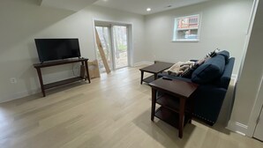 A living room with a flat-screen TV on a wooden stand, a dark blue sofa, and a small table. - Newly Renovated Lakefront Home with Kayaks and Paddleboards (Locust Grove)