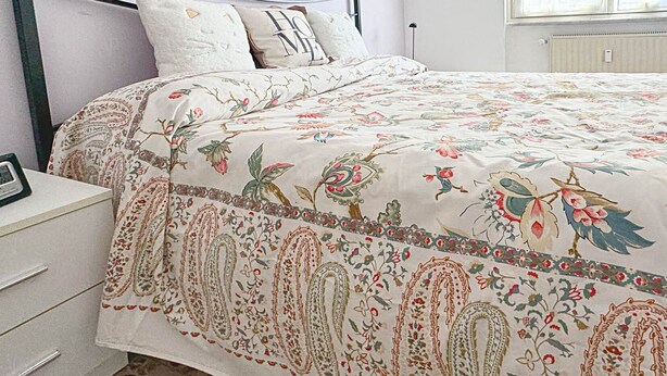 A bedroom with a floral bedspread, a bedside table with a clock, and a radiator on the wall. - Casa Albachiara a 500 Metri Dalla Spiaggia (Lavagna)
