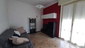 A living room with a sofa, a TV, a bookshelf, and a red accent wall. - Casa Albachiara a 500 Metri Dalla Spiaggia (Lavagna)