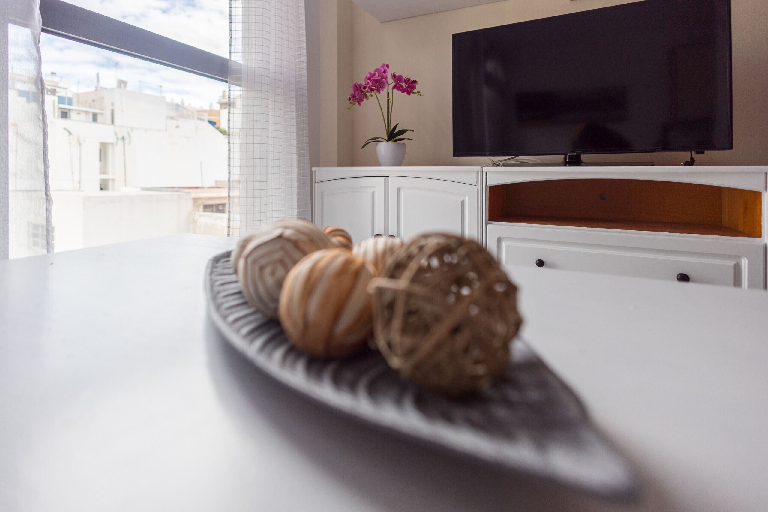 A modern living room with a flat-screen TV, a potted orchid, and a decorative plate with macaron-style cookies.