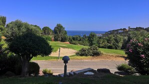 Eine Küstenlandschaft mit freiem Blick auf das Meer, einer Straße mit Schutzrail und verschiedenen Bäumen und Sträuchern.