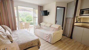 Ein Schlafzimmer mit zwei Betten, einem Fernseher, einer Küchenzeile und einem Balkon mit Vorhängen.