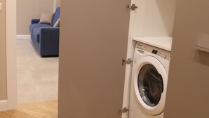 A compact laundry room with a washing machine, wooden flooring, and a blue sofa in the background. - Freedom holiday house Positano (Sant'Antonio Abate)