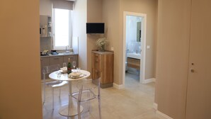 A compact kitchen with modern appliances, a dining area with clear chairs, and a flat-screen TV mounted above the counter. - Freedom holiday house Positano (Sant'Antonio Abate)