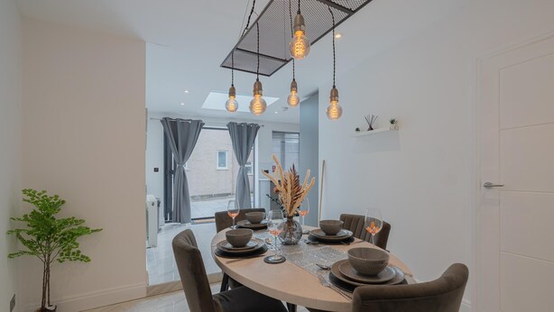 A dining area with a round table set for four, surrounded by chairs. There are hanging light fixtures above the table, and a potted plant is visible to the left. - Stunning 3 Bedroom House-tottenham Stadium-parking (London)