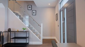 A modern interior with a staircase, a black metal console table, a cushioned bench, and a door. - Stunning 3 Bedroom House-tottenham Stadium-parking (London)