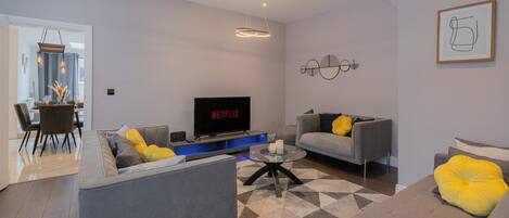 A modern living room with a grey sofa, a coffee table, and a flat-screen TV displaying 'NETFLIX'.