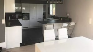 A modern kitchen with white cabinets, a black countertop, and a dining area with a white table and chairs. - Maison Récente T5 Herbignac Proche Guerande (Herbignac)