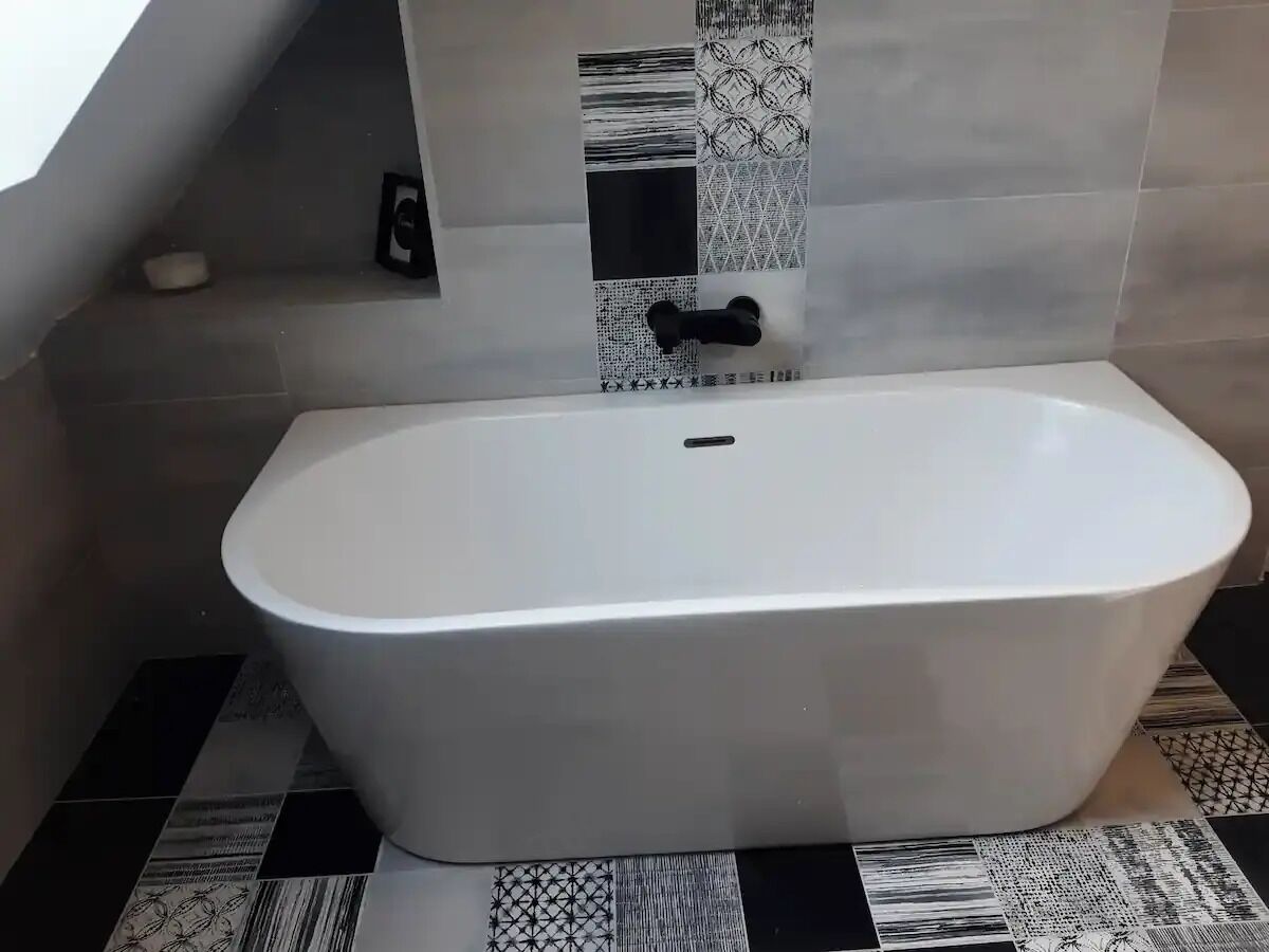 Une salle de bain moderne avec une baignoire sur pieds, des carreaux décorés et une petite étagère sur laquelle se trouve une bouteille.